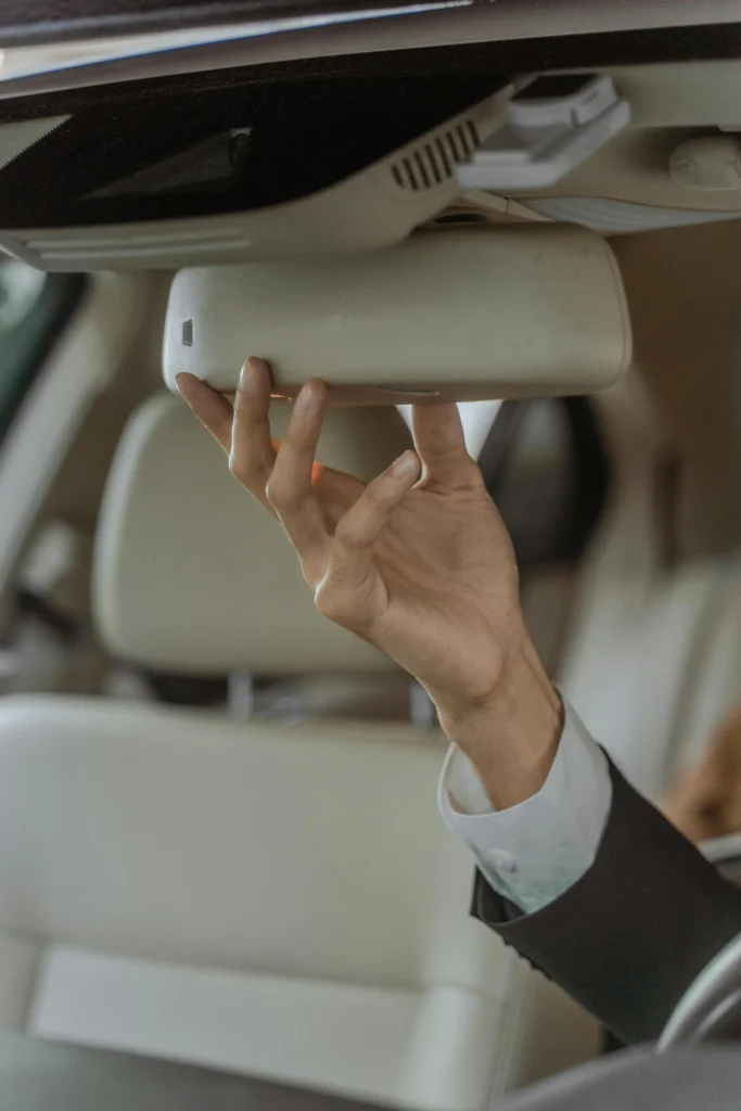 A professional chauffeur in a suit adjusting the rear-view mirror in an elegant car interior, focusing on precision and safety.