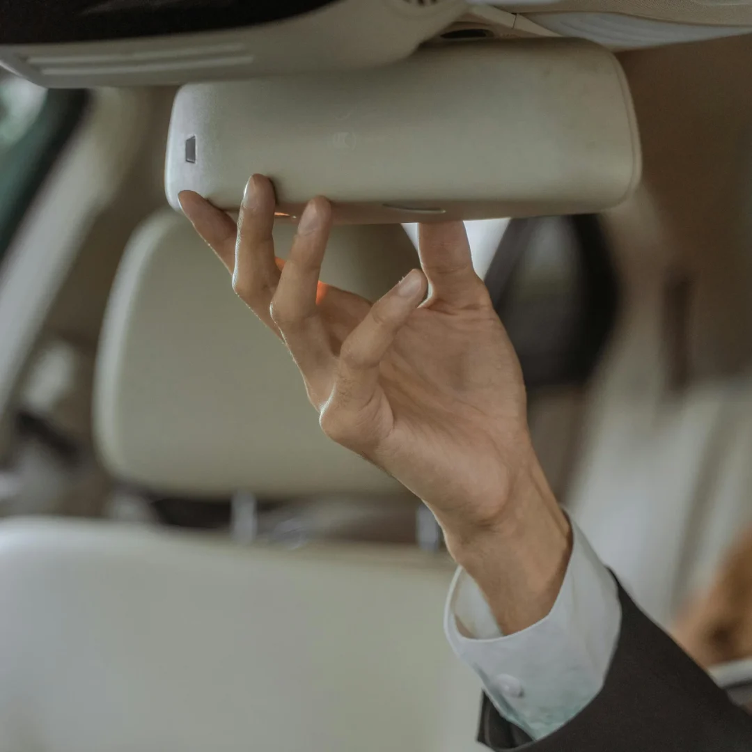 A professional chauffeur in a suit adjusting the rear-view mirror in an elegant car interior, focusing on precision and safety.